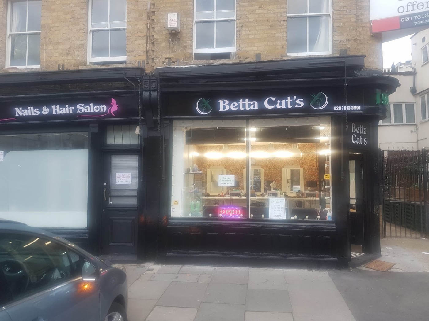 The Betta Cut's Barber's shopfront on Hoxton Street, black frontage, green sign and the lit interior with mirrors and styling chairs.