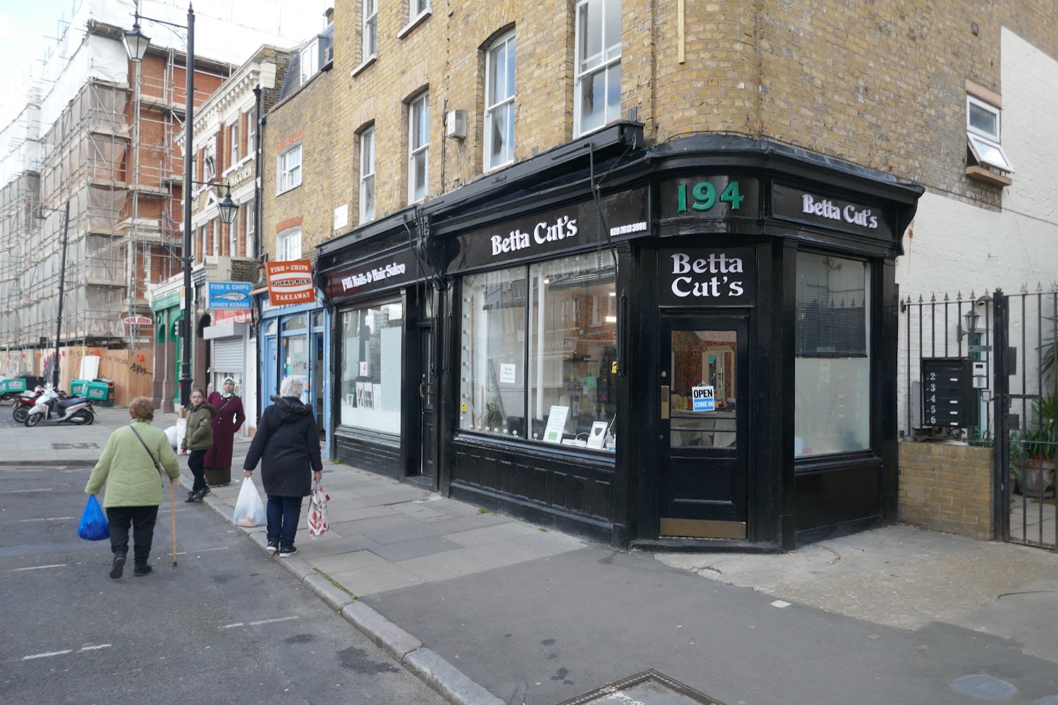 Hoxton Street in daylight with the Betta Cut's Barber's corner shop and neighbouring shops and market stalls.